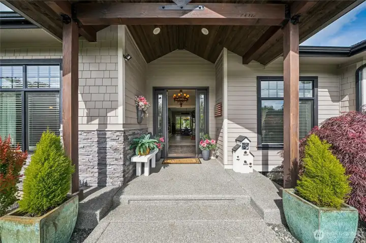The distinctive front exterior showcases a welcoming covered entry porch, highlighted by a richly detailed timber-lined ceiling and beams that adds warmth, texture, and architectural character. The distinctive front exterior showcases a welcoming covered entry porch, highlighted by a richly detailed timber-lined ceiling and beams that adds warmth, texture, and architectural character.