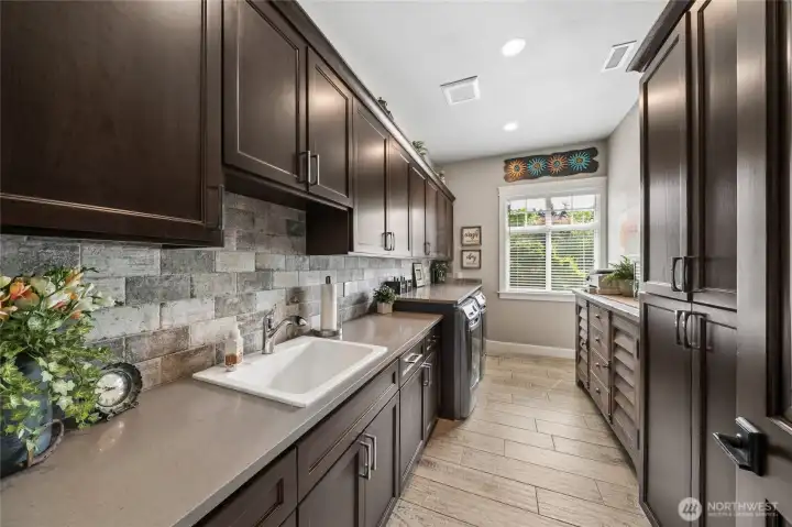 Expansive utility and laundry room showcasing an exceptionally generous layout, complete with abundant cabinetry, extensive countertop workspace, a utility sink, and front-load washer and dryer. Expansive utility and laundry room showcasing an exceptionally generous layout, complete with abundant cabinetry, extensive countertop workspace, a utility sink, and front-load washer and dryer.