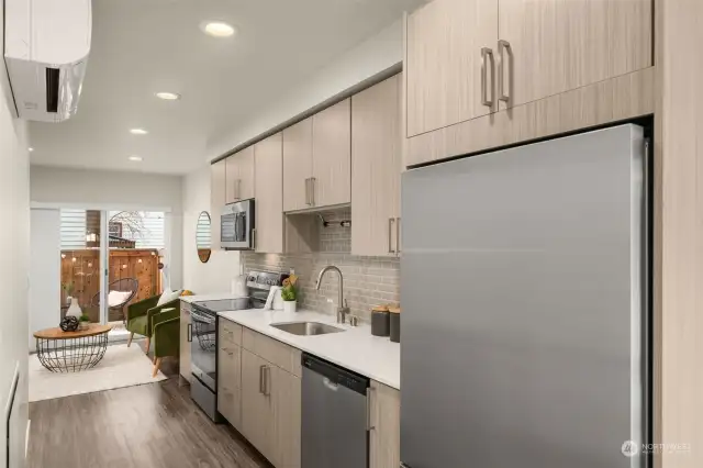 The lower-level open-concept living area free flows into a chef’s kitchen, accompanied by warm-toned cabinetry, quartz countertops, and stainless-steel appliances.