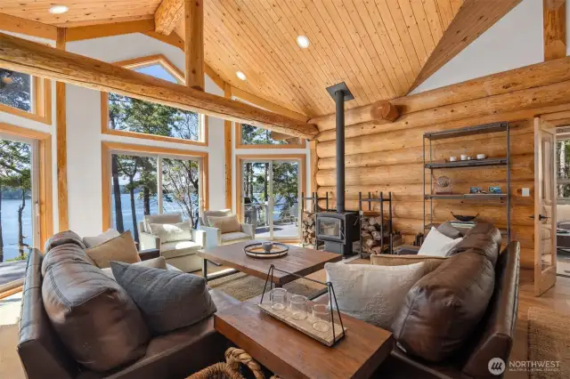 Living room with soaring ceilings and expansive windows floods the space with light and offers uninterrupted views of the water, framed by hand-hewn log beams.