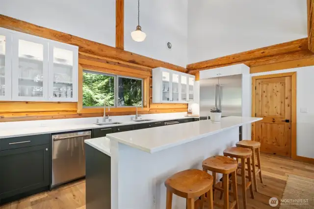 High-end stainless steel appliances, dual prep sinks, and expansive stone countertops make this a chef’s dream, complemented by views of the ocean framed by handcrafted log detail.