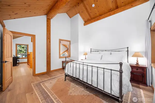 Soaring cedar ceilings and exposed beams highlight the refined craftsmanship of one of two upper level bedrooms. Expansive wall space and peaceful forest views create a calm, luxurious retreat.