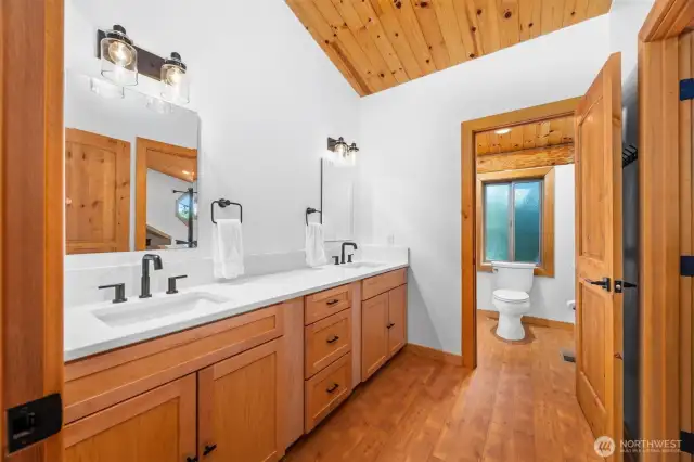 This spa-inspired jack and jill upper level bathroom features a custom dual-sink vanity with sleek matte black fixtures, quartz counters, and clean-lined cabinetry. A private water closet and natural wood finishes elevate the serene design.