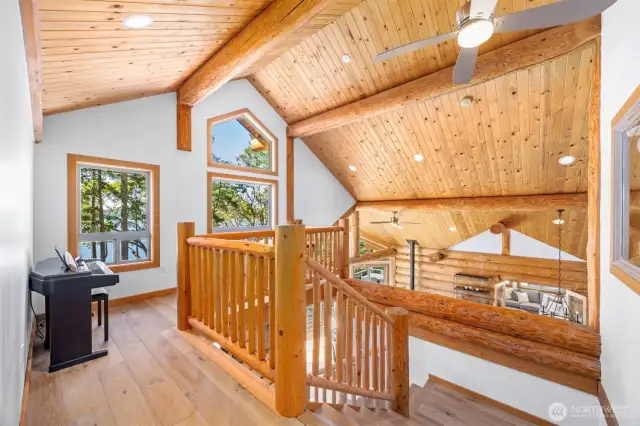 Sweeping staircase with exposed log beams, soaring ceilings, and oversized windows that frame the serene water views, delivering a grand entrance with architectural drama.