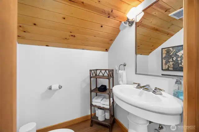 Tucked beneath a pitched roofline, this charming half-bath on the main level combines simplicity and elegance with a pedestal sink and warm wood accents.