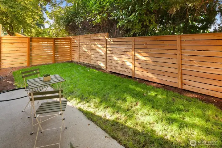 Fully fenced and level backyard with mature trees and patio.