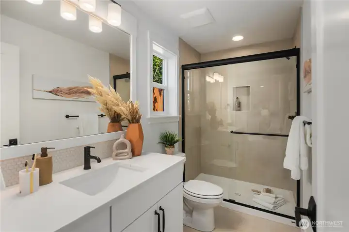 Lower Level Ensuite Bath: Thoughtfully designed en-suite bath offers a quartz-topped vanity, framed mirror, and a walk-in shower with full-height tile surround. Conveniently located off the lower-level suite, it ensures both style and privacy for guests.  Staged photos are of the model home of the same floorplan within the Foxmoore community and are for visualization purposes only. Colors, finishes, and layout can and will vary.