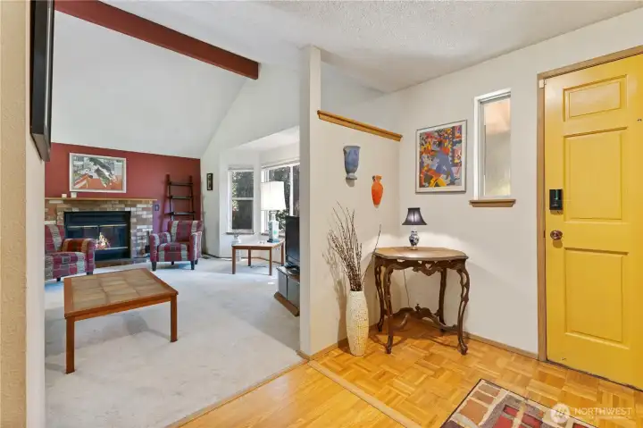This entryway features a dedicated space that leading into a spacious living room highlighted by vaulted ceilings with exposed wood beam. Three large windows bathe the room in abundant natural light, perfectly accentuating the cozy brick-surround wood fireplace.