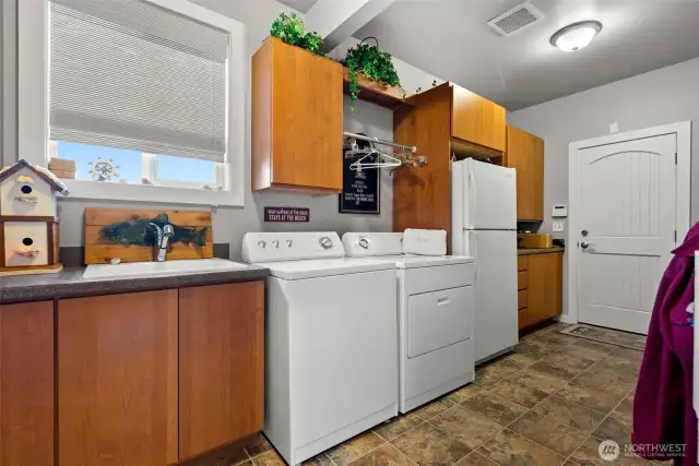 Nice laundry and mud room set up with sink, laundry cabinetry, extra fridge and space for all your coats