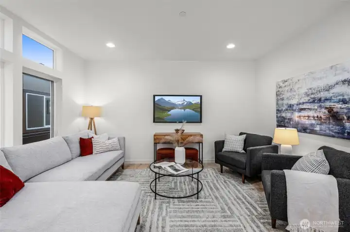 A bright and inviting living room perfect for gatherings or quiet evenings, this space offers ample relaxing room, highlighted by natural light streaming through oversized windows. Photos of home with similar layout, finishes & fixtures.