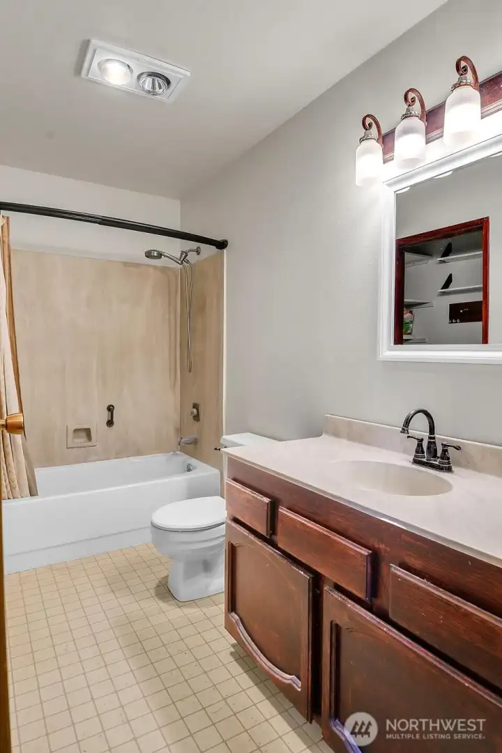 Well-lit full bath has a large vanity with drawers and cabinets for personal storage space.