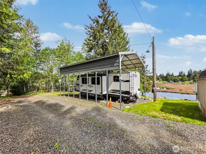 Side view of RV and carport with gravel access and lake nearby