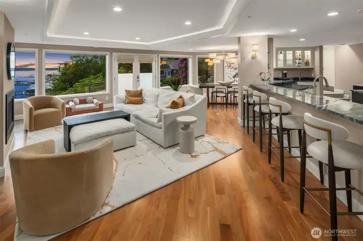 This is the heart of the home — where the lake view draws you in and the open plan invites you to stay. The marble island transitions seamlessly from the living room to the kitchen, with bar seating, a built-in bar cabinet, and lush greenery framing the windows at every turn. Sophisticated, warm, and built for the way you actually want to live.