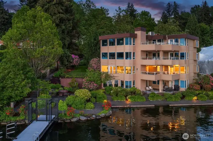 Reflected in the still waters of Yarrow Bay, the home announces itself with quiet confidence — warm light spilling through walls of glass, two decks and a riot of color from blooming rhododendrons and manicured grounds that lead gently to the water's edge. Level entry, a private lawn, and a gated dock just steps below. Welcome to one of Kirkland's most coveted addresses.
