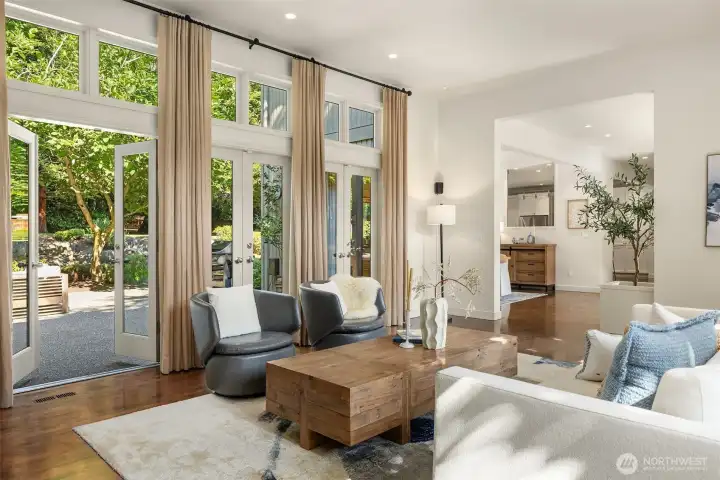 Light-filled living with walls of windows & glass French doors opening up to the backyard
