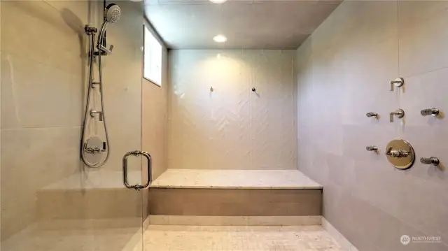 Spa-inspired steam shower with his and hers shower heads, four body jets, rain dome all highlighted by Carrara marble tile floor and bench.