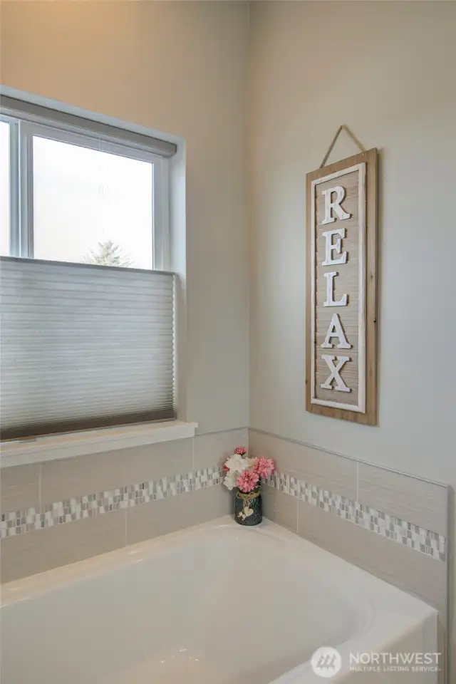 Stepping into the primary bathroom, the large soaking tub is on the left, with a view window to enjoy while you relax!
