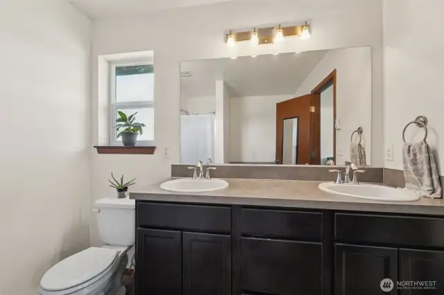Two sinks for all your beauty needs, plus a window that brings in natural light. Perfect for getting your makeup just right, or for anyone who prefers a better view in natural light. Add in dark shaker cabinets, sleek overhead lighting, and that large mirror, and this bath is ready for anything.