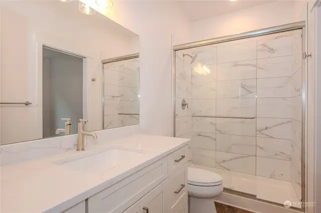 The Guest Bathroom boasts a sizable vanity with gorgeous quartz counters and a full tile shower with a sleek sliding glass door.