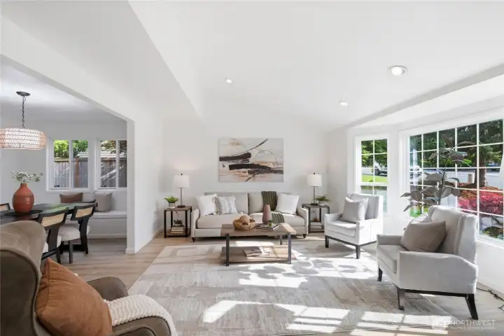 Sunlit and spacious living room featuring light hardwood-style floors, recessed lighting, and an open connection to both the dining nook with built-in bench seating and the backyard.