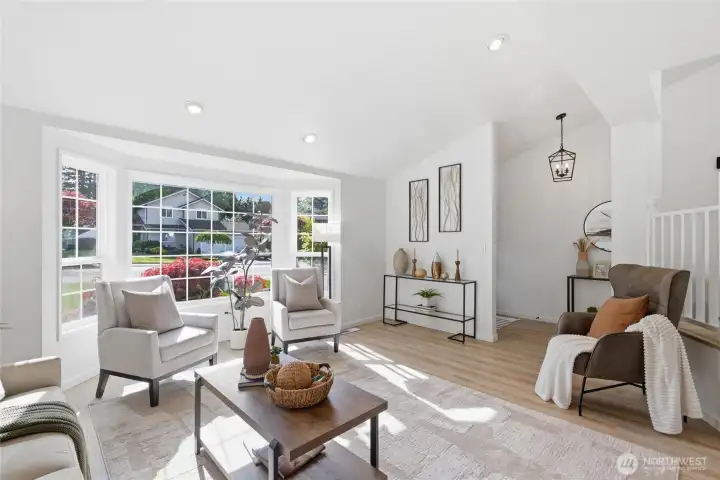 A sun-drenched sitting area anchored by a large bay window with garden views, recessed lighting, and easy access to the entry — ideal for relaxing or entertaining.