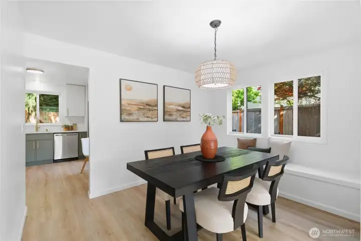 Inviting dining area with a designer pendant light, built-in bench seating, and windows overlooking the backyard — opens directly to the updated kitchen with sage green cabinetry and stainless appliances.