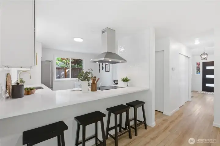 A white quartz peninsula with seating for four anchors the kitchen and creates a natural gathering spot, with a statement range hood above and a sightline to the front entry.