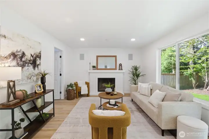 A wider view of the family room showcases the full space — brick fireplace, large picture window, backyard slider, and warm hardwood-style floors throughout.