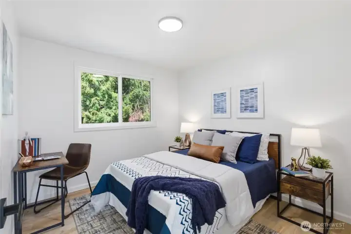 Comfortable secondary bedroom with a tree-lined window view, warm hardwood-style floors, and a clean neutral palette.