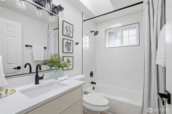 Beautifully updated full bath with quartz countertop, matte black fixtures, subway tile tub surround, and an industrial-style vanity light — sharp, clean finishes throughout.