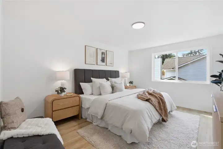 Spacious primary bedroom with a neutral palette, warm hardwood-style floors, and a large window — a calm, restful retreat.