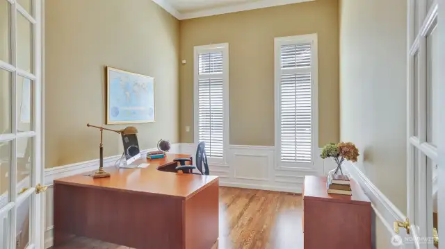 Main level den is light and airy featuring wainscot and crown molding details, lofted ceilings, and French doors.