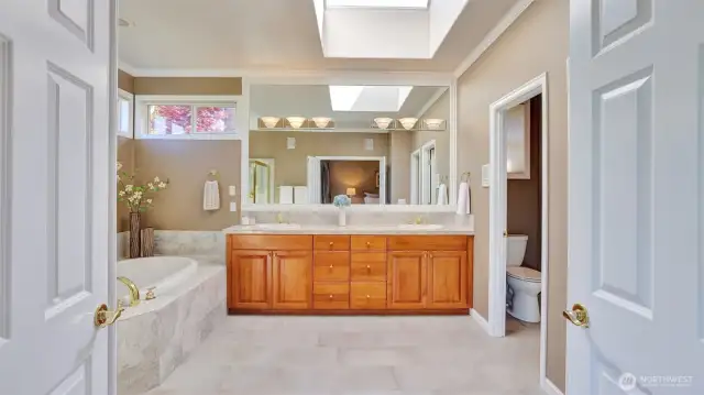 En suite off the primary bedroom showcases dual vanities, skylight, and a large walk-in closet with custom built-ins.