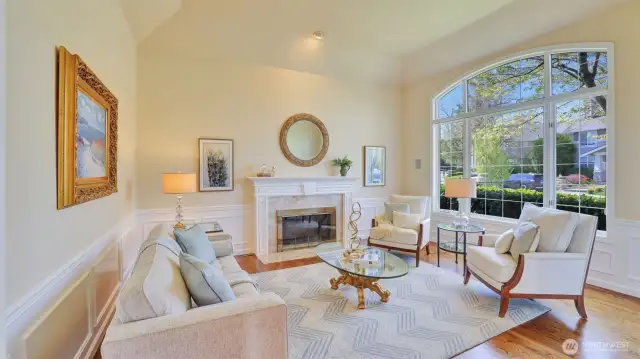 Living room with coffered ceiling, arched sun-lit windows, and marble surround gas fireplace.
