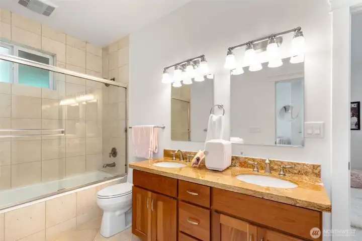 This full bath is between the two bedrooms and features a double vanity with stone slab counters and a stone tile tub/shower.