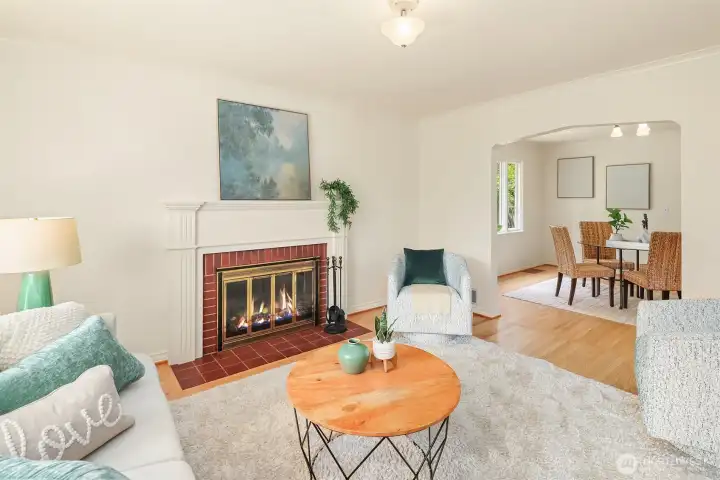 Sunny, spacious living room with gleaming oak hardwood floors and an inviting wood fireplace and the dining room in the background