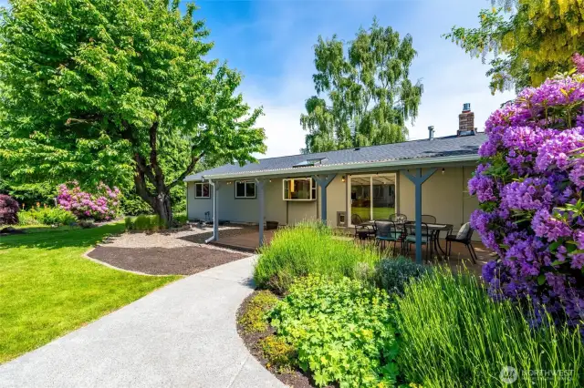 Park-like setting in your large yard with many different gardens. This covered back deck is on the main house. Paved walkways are available from both the driveway and the back deck to get to the other buildings (shop/studio/ADU).