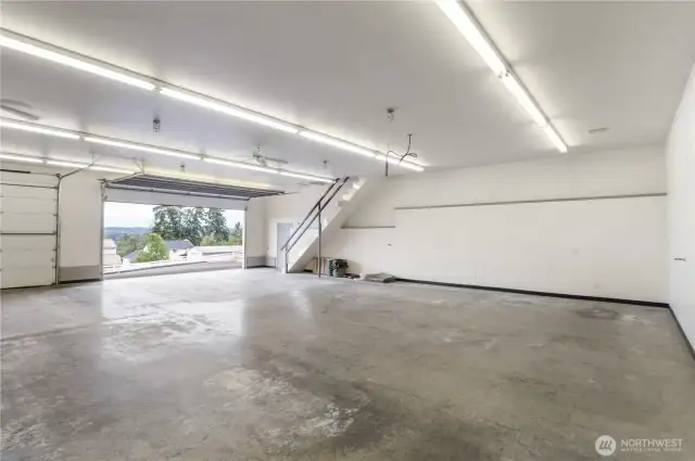 Part of the huge heated 2,995 sq ft shop. Walls to the right have numerous plug-ins for florescent lights and other fun signs. Notice diamond plated stairs near opened front garage door, leads up to next picture