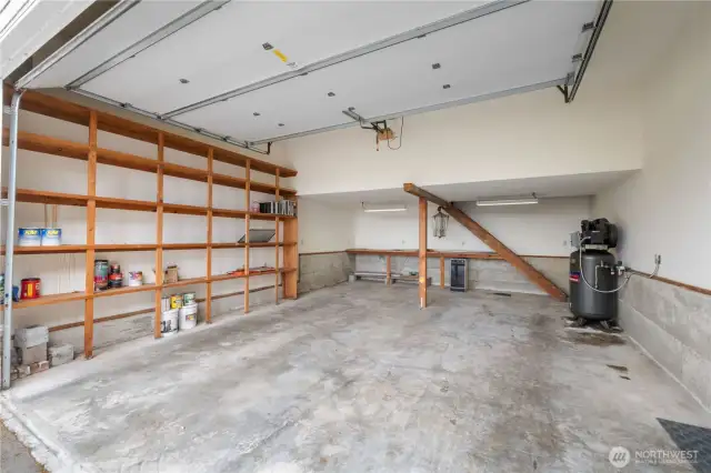 Left 2 car side of 3 car garage with shelving on the left and stairs leading up to storage area