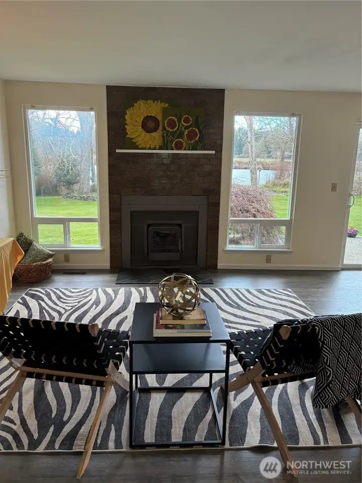 Living room features grand picture windows and wood stove for cool evenings, vinyl plank flooring throughout.
