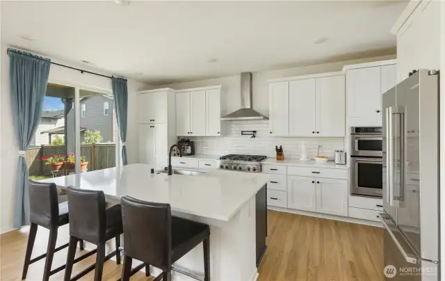 Builder upgraded kitchen to their top of the line model. Double ovens, 6 burner gas stove with tile backsplash, stainless hood and pot filler. Lots of storage, a walk-in pantry (out of frame on the right), a huge island and sliding door to the backyard covered patio.