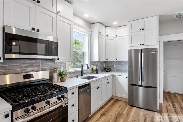 View from Kitchen entry showing new white shaker cabinets, quartz countertops, stainless steel appliances and ceramic tile backsplash