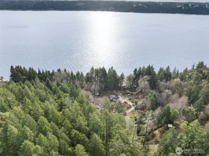 Aerial view showing the full 1-acre hillside layout with multiple leveled areas, established driveway access, cleared pads, and forested surroundings. Property backs directly to DNR land for added privacy.