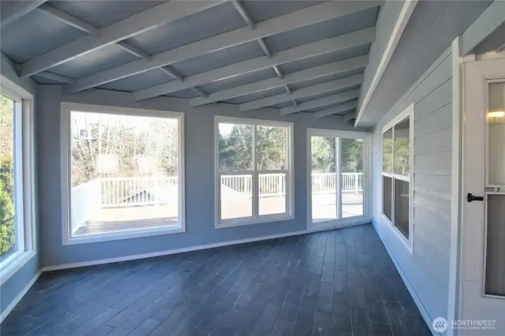 spacious sunroom with abundant window, connected family room and sliding door leading to the backyard deck