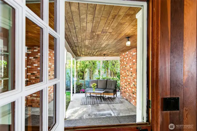Seen through vintage windows, the covered patio beckons—cloistered in cedar and brick, yet open to sky and greenery. A perfect perch for morning coffee or evening unwinding, this peaceful portal blurs the line between indoors and out, anchoring the home in timeless Browns Point character and coastal calm.