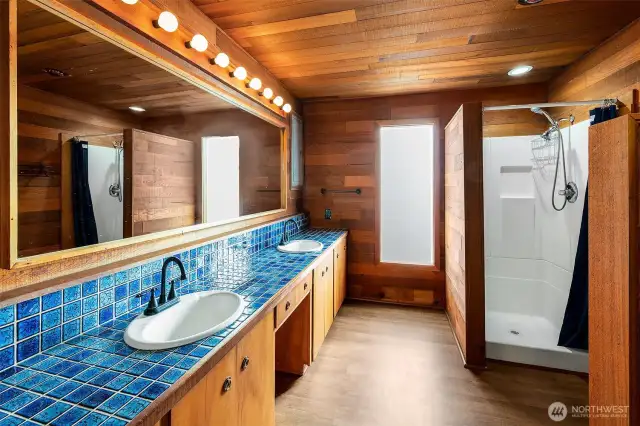 Wrapped in cedar paneling and grounded by handcrafted cobalt tile, this bath evokes the cozy calm of a Nordic spa. Dual sinks, warm wood textures, and a walk-in shower offer both utility and retreat—an ideal setting to begin or end the day above the glimmering waters of Caledonia Cove.