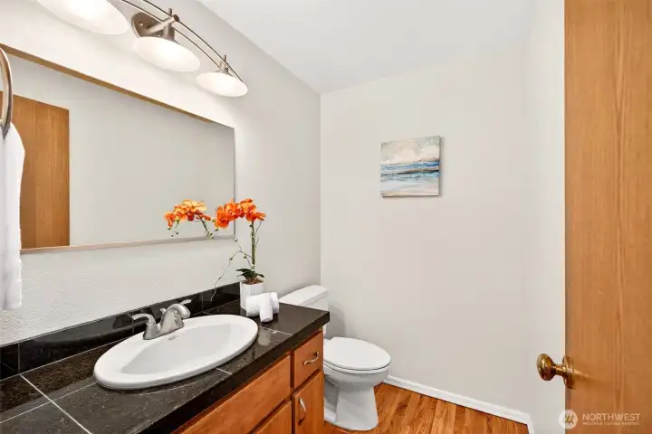 Convenient main level half bath with a large mirror, updated lighting, and a stone topped vanity that offers extra counter space. A great everyday feature for guests and daily routines.