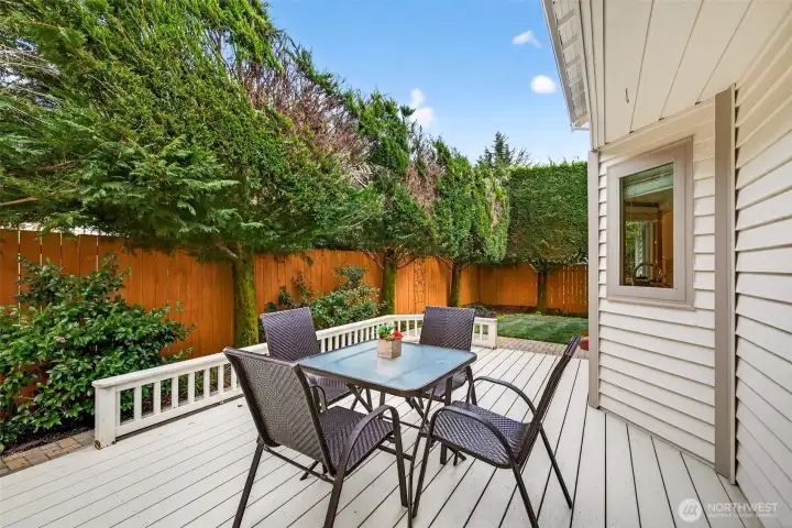 Outdoor dining on the deck set against a backdrop of mature evergreens and full fencing, creating a private setting for grilling, entertaining, and enjoying summer evenings. The layout offers room for multiple uses, from dining to a separate lounging zone.