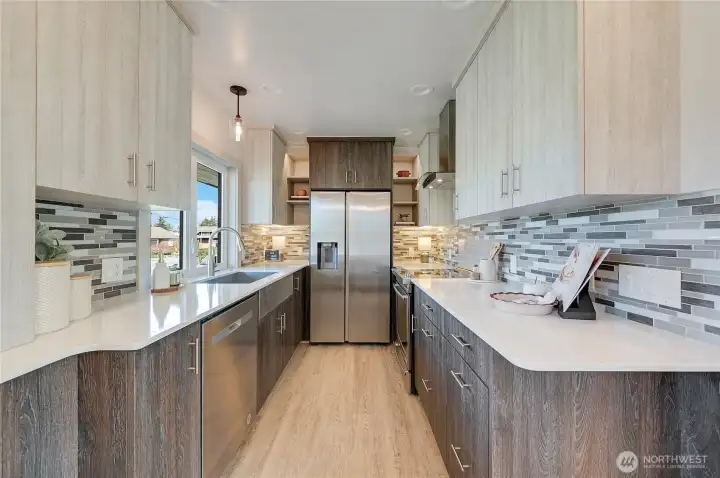 Galley style kitchen with stainless steel farm sink and appliances, solid surface counter tops, ceramic tile back splash. Main water shut-off located under kitchen sink  Book sheves by refrigerator have upper shelf twinkle lights.