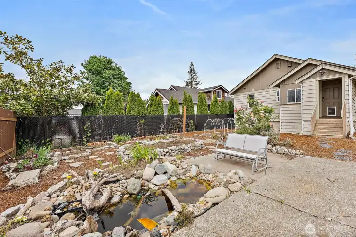 Private backyard retreat features mature landscaping, patio space, and a peaceful pond creating a relaxing outdoor setting.
